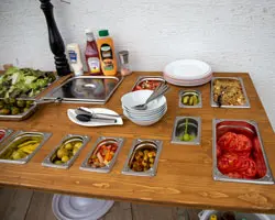 In den Abschnitt dem großen Gastronomie-Behälter der Größe 1/1, welcher mit Tomaten gefüllt ist, würden auch vier kleine mit der Größe 1/3 Behälter passen. Auch, wenn die Aussparungen der Theke nicht verändert werden können, ist eine unterschiedliche Bestückung jederzeit möglich. Theke mit GN-Behälter